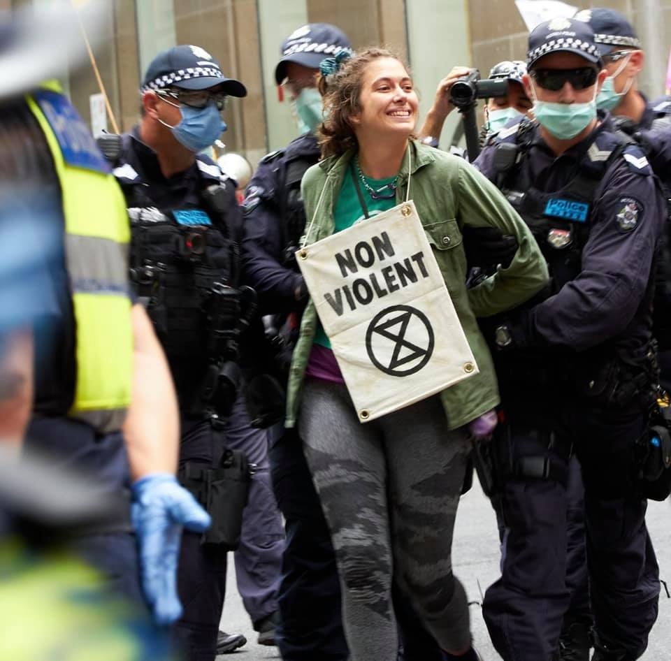 Violet Coco wearing a sign saying, "Non Violent", being arrested at an earlier protest.